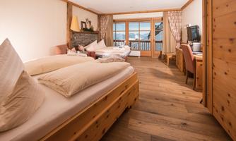 A cozy bedroom with wooden furniture and two beds. Large windows offer a view of the mountains.