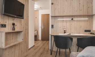 A modern room with wooden walls and a television on the wall. The workspace features a desk and two chairs.