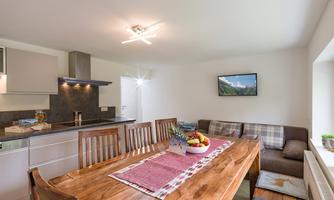 A modern dining room with a large wooden table and comfortable chairs. The kitchen is well-equipped and the room is bright and inviting.