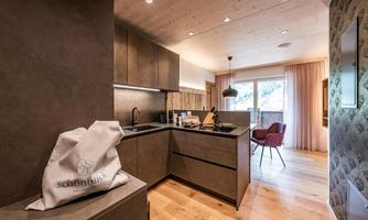 A modern kitchen with wooden flooring and elegant interior. Through the window, there is a view of the outdoor area.