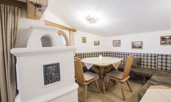 A cozy dining area with wooden chairs and a table. The walls are decorated with pictures and a heating chamber provides warmth.