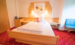 A cozy room with a double bed and red carpet. On the wall, there is a picture and two bedside lamps.