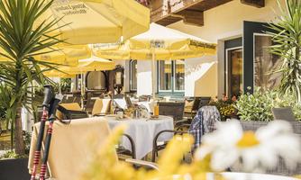 A cozy outdoor area of a café with sunny yellow umbrellas. There are tables, chairs, and blooming plants that create an inviting atmosphere.
