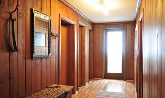 A cozy hallway with wooden paneling and several doors. Light streams through the glass door at the end of the hallway.