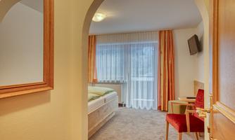 A cozy hotel room with a large window and elegant furnishings. The room features a bed, an armchair, and a television.