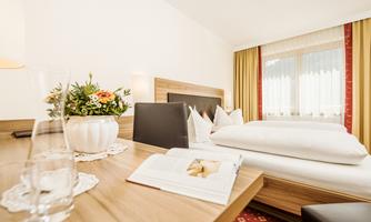 A cozy room with a comfortable bed and warm colors. On the table, there is a flower vase and an open book.