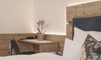 A cozy room with a bed and a small desk. On the table sits an orchid in a pot.