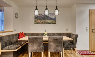 A modern dining room with a large wooden table and cozy chairs. The walls are bright, and a landscape painting enhances the atmosphere.