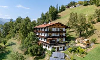 A charming wooden house surrounded by green meadows and trees. The view of the gentle hills in the background is picturesque.