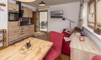 A cozy apartment with modern furniture and a wooden dining area. The decor includes a red couch and an open kitchen.
