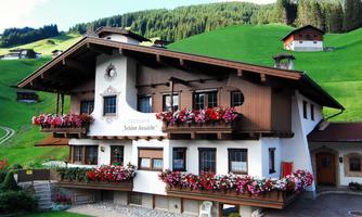 A traditional chalet with blooming balcony boxes. The surroundings are surrounded by green hills and trees.