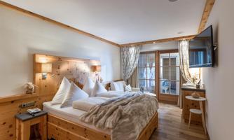 A cozy bedroom in alpine style with wooden paneling and a large window. The beds are inviting and covered with soft blankets.