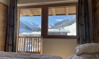 A cozy bedroom with a view of snow-covered mountains. Bright light flows through the windows, creating an inviting atmosphere.
