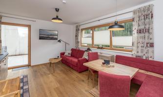 A cozy living room decor with red furniture and wooden flooring. Large windows provide plenty of daylight and connect the interior with the outdoor area.