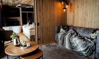 A modern room with wood paneling and a cozy sofa. A small seating area with a table and decorative elements completes the stylish decor.