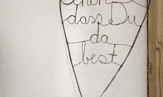 A wire-made heart hangs on a wall. It says: "Glad you're here."