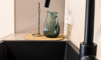 A modern kitchen corner with a black faucet and a stylish sink. On the countertop, there is a green pitcher and a decorative stand.