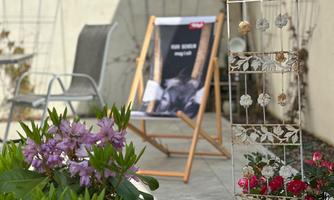 A cozy outdoor area with flowers and a deck chair in the background. A poster with an animal motif hangs on the wall.