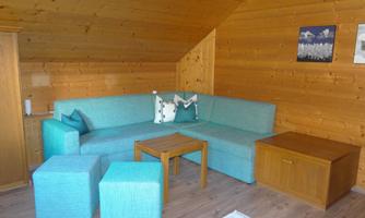 A cozy living room with a turquoise sofa and wooden walls. There is a small table and additional seating.
