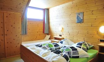 A cozy bedroom with wooden paneling and two beds. The bedding is colorful, and there is a small bedside lamp.