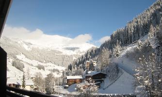 A snowy mountain landscape with charming wooden houses. The sky is clear and blue, while the trees are covered with snow.