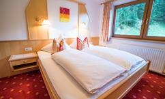 A cozy bedroom with a double bed and soft pillows. The window offers a view of greenery and creates a bright atmosphere.