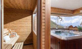 A modern wellness area with a sauna and a whirlpool.  
Large windows offer a beautiful view of the surrounding mountains.