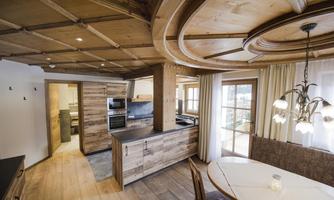 A modern kitchen with wooden paneling and a round dining table. Large windows provide plenty of daylight and create a cozy atmosphere.