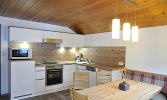 A modern kitchen with a wooden ceiling, white cabinets, and modern appliances. A table with chairs invites you to dine.