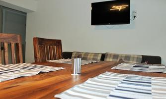 A dining room with a wooden table and two chairs. A television is hanging on the wall, and striped placemats are lying on the table.