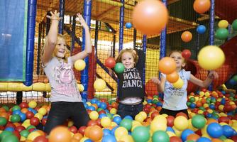 Three happy children are playing in a colorful ball pit. They are throwing colorful balls into the air and having a lot of fun.