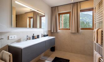 A modern bathroom with a large mirror and a stylish sink. There are windows with a view of the mountains and bright curtains.