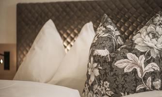 A cozy bed with decorative pillows and an elegant headboard covering. The pillows are in soft colors and give the room a warm atmosphere.