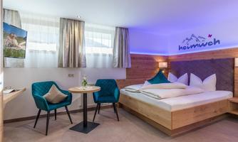 A modern hotel room with wood interiors. There is a large bed, a small table with chairs, and a television.