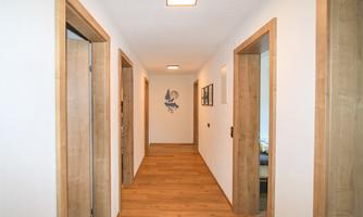 A bright hallway with wooden flooring and white walls. Doors on the left and right sides create an inviting atmosphere.