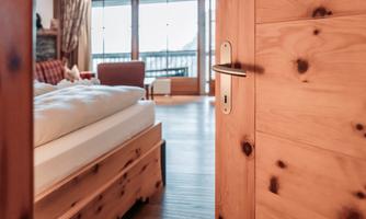 A cozy bedroom with a wooden bed and a view of a balcony. The warm colors and natural light create an inviting atmosphere.