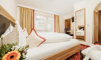 A cozy hotel room with a large bed and decorative pillows. The windows are adorned with curtains, and a mirror is in the room.