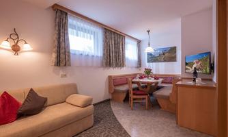 A cozy living space with a beige sofa and a dining table. Large windows let in plenty of light, and the decoration is friendly and inviting.