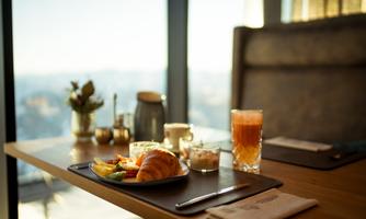A laid table with breakfast on a tray. It includes a croissant, fresh fruit, and drinks with a view of the city.