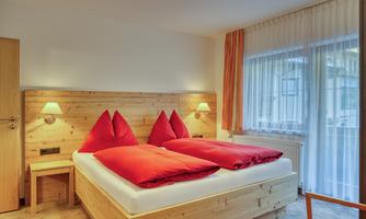A cozy bedroom with a double bed and red pillows. Large windows let in plenty of natural light.