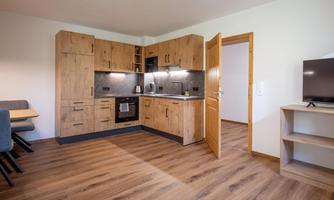 A modern kitchen with wooden cabinets and a cozy dining area. The room is bright and inviting with a television in the corner.