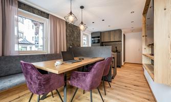 A modern dining area with a large table and purple chairs. The room features plenty of natural light and a stylish decor.