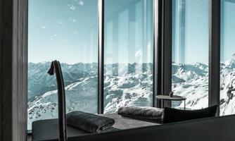 A modern bedroom with large windows and a breathtaking view of snow-capped mountains. The room exudes tranquility and elegance.