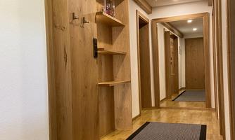 A narrow hallway with wooden paneling and bright lighting. The floor is covered with a modern rug, and there are coat hooks on the wall.