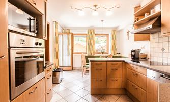 A modern kitchen with wooden cabinets and white walls. It has large windows that let in plenty of light.