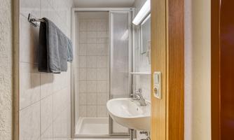 A small bathroom with a shower and a sink. Towels hang on the wall and the tiles are bright.