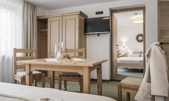 A cozy room with wooden furniture and a table. In the background, another bedroom is visible.