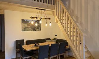 A cozy dining area with a large table and chairs. A modern wooden staircase leads to the upper area.