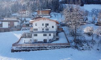 A modern house in a snowy landscape. Surrounded by trees and other buildings, it showcases an idyllic winter atmosphere.