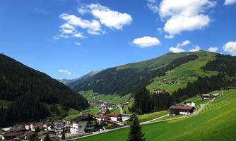A picturesque mountain landscape with green hills and a small village in the valley. The sky is clear with a few clouds.